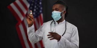 戴着冠状病毒口罩的非洲裔美国男性科学家在新闻发布会上展示Covid-19疫苗，闪光灯闪烁。自信的医生用语言和手势宣传药物。