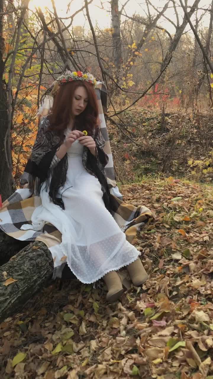 红发女人在秋天的森林里坐在圆木上。