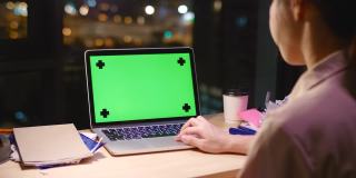 女人在晚上使用绿色屏幕的笔记本电脑