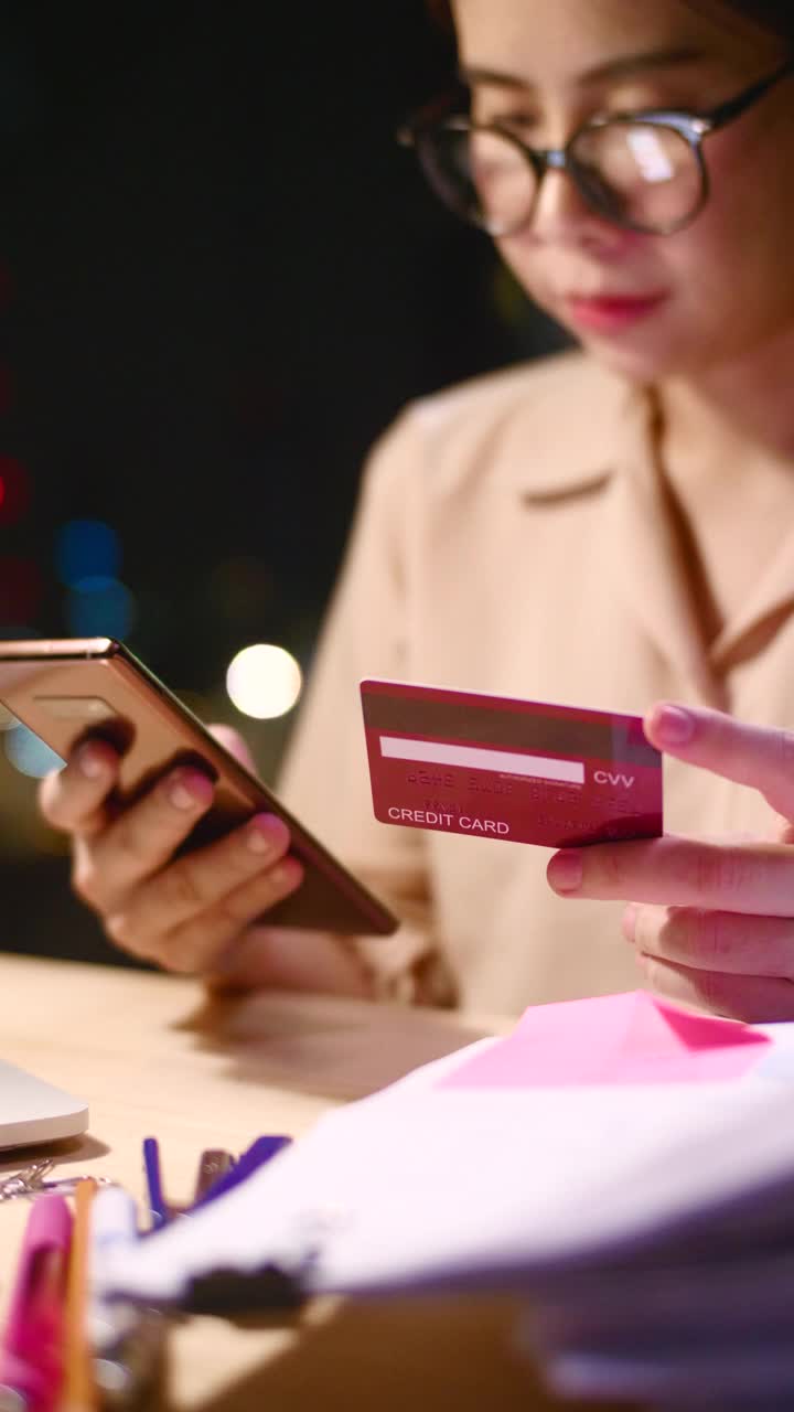 一名年轻女子在工作间隙用智能手机和信用卡在网上购物