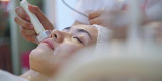 女性与美丽的皮肤正在被按摩师在一个放松的心情面部按摩。水疗中心的按摩师们正在给脸部敷面膜，以恢复活力和面部护理。