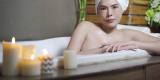 浴缸里点着蜡烛的性感女人。放松的女人泡在肥皂浴里，在装饰着蜡烛的健康水疗概念的按摩浴缸边睡觉。