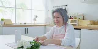 亚洲活跃的老年妇女和年轻的女儿在花瓶上插花。漂亮的奶奶和漂亮的孙女在家里装修厨房时感到很开心。家庭活动关系