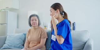 亚洲护士在养老院照顾残疾老年妇女。美丽的治疗师医生在沙发上用听诊器测量女性老年病人的心率。医疗保险服务理念。