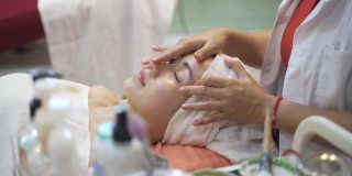 女性与美丽的皮肤正在被按摩师在一个放松的心情面部按摩。水疗中心的按摩师们正在给脸部敷面膜，以恢复活力和面部护理。