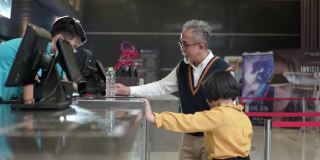 亚洲的中国爷爷孙女在电影院放映前用非接触式付款购买爆米花