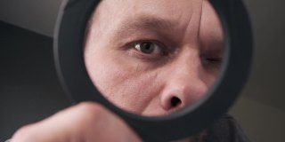 一个中年男人透过放大镜看照相机的眼睛。幽默的