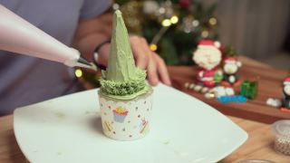 高视角:亚洲妇女的手从奶油榨汁机中榨取绿色奶油，在自制的圣诞树上做成树叶，作为庆祝圣诞节的甜点，12月假日在公寓里装饰圣诞树，礼盒，圣诞老人。视频素材模板下载