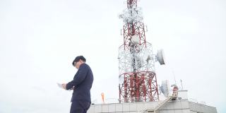 身穿西装、手持平板电脑站在电信塔屋顶的快乐亚洲商人