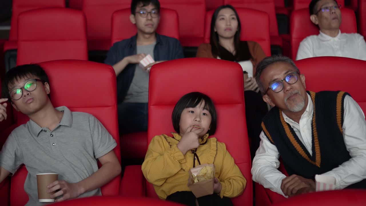 一位亚洲华人爷爷和他的孙子们喜欢在电影院看电影。