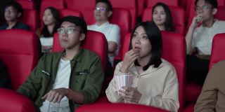亚洲的中国年轻夫妇在电影院等待电影放映时分享食物，享受彼此的陪伴