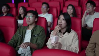 亚洲的中国年轻夫妇在电影院等待电影放映时分享食物，享受彼此的陪伴视频素材模板下载