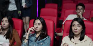 坐着看电影的亚裔中国女性朋友，一对夫妇进入电影院晚了，经过他们去找座位