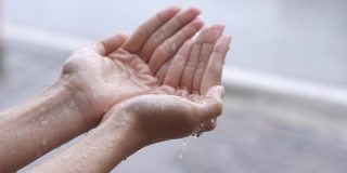 一名女子在热带台风造成的雨天用手抓着雨点，享受着清纯的春雨天气，享受着泼洒着纯净的水滴，人们触摸着大自然，站在路边
