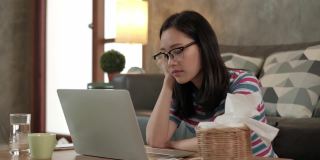 亚洲妇女在家工作，在笔记本电脑后面打盹和打瞌睡。