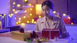 年轻的成年快乐的亚洲女人购物在家里的圣诞礼物盒，而坐在家里的客厅在晚上视频素材模板下载
