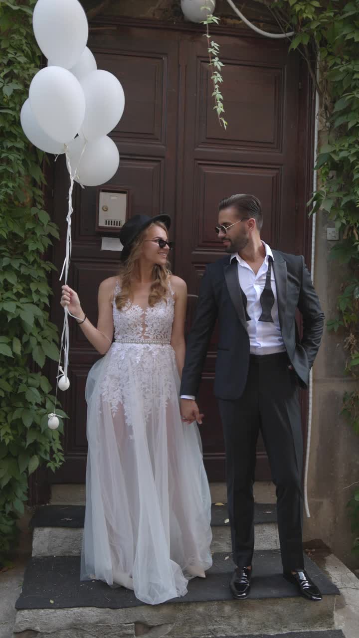 微笑的新郎和新娘站在乡村的门前，手里拿着气球和香槟
