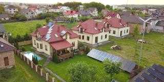 鸟瞰图的郊区住宅和私人住宅与绿草覆盖的院子，太阳能电池板的屋顶，游泳池与蓝色的水和风力发电机。