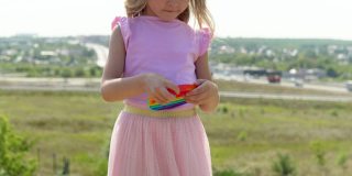 一个穿粉红色裙子的女孩扮演popit。孩子热衷于彩虹抗压力。孩子的硅胶玩具