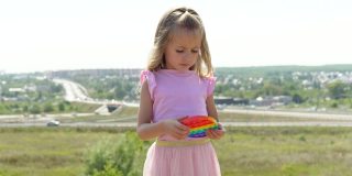 一个穿粉红色裙子的女孩扮演popit。孩子热衷于彩虹抗压力。孩子的硅胶玩具