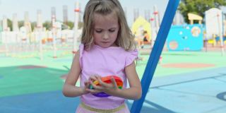 一个穿着粉红色裙子的女孩在操场的背景上玩起了小游戏。孩子热衷于彩虹抗压力。孩子的硅胶玩具