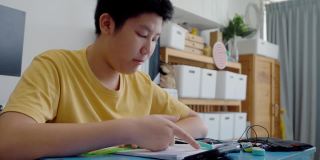 亚洲男孩一边做作业一边在家学习在线课程，社交距离的生活方式概念。