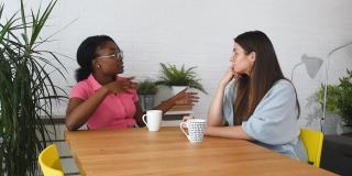 在一家网络开发公司工作的两位年轻同事，一位黑人女性和一位白人女性坐在一起喝咖啡休息，谈论他们的私人生活和未来计划，选择性地聚焦