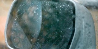 一辆车在雨中的侧后视镜，雨点落在侧后视镜和车窗上