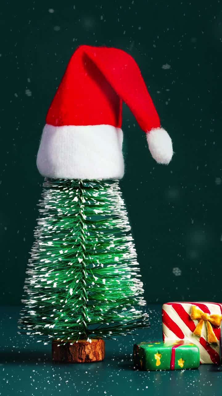 圣诞快乐和新年快乐雪花飘落，绿色松树上的圣诞帽和深绿色背景上的礼盒。节日庆祝贺卡