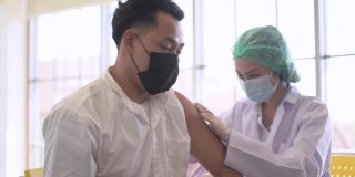 图为一名亚洲男子在诊所或医院接种新冠疫苗时通过手机自拍，护手注射疫苗以获得免疫力以保护病毒。人们戴着防护口罩。