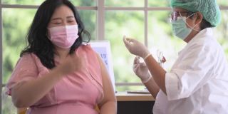 图为一名亚洲女性在诊所或医院接种新冠疫苗时的自拍照片，护工正在注射疫苗以获得保护病毒的免疫力。人们戴着防护口罩。