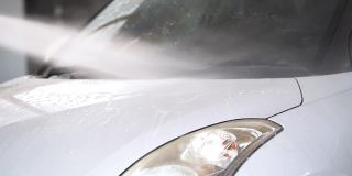 水雾正在清洗一辆白色汽车。在车库封闭水喷清洗车辆前车裙部。工人使用水喷淋车辆。