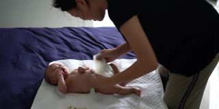 亚洲母亲在床上给孩子换尿布