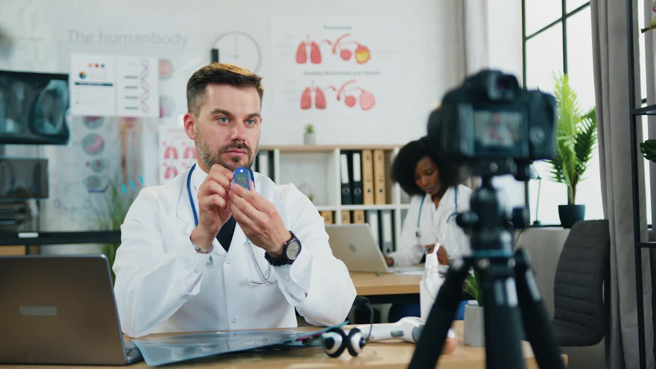 远程医疗的概念，英俊自信聪明经验丰富的胡子医生通过摄像机向在线观众解释如何使用脉搏血氧计
