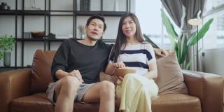 亚洲成人恋人结婚夫妇享受在沙发沙发上看电视，一起在家里享受宁静和幸福，居家隔离的生活方式