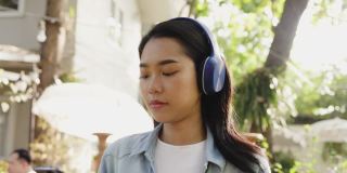 年轻美丽的亚洲女人戴着耳机从智能手机音乐微笑快乐的夏天花园。少年是快乐的周末。假日旅行。生活方式的概念