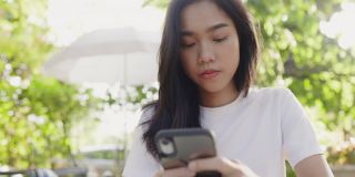 美丽的亚洲少女在社交媒体上用智能手机开心地微笑在夏季花园。在手机触摸屏上给家人写祝福信息。社会网上购物。在家网上订购