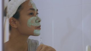 中年亚洲女性居家浴室，在镜子前用泥、泥或护肤品做面膜，以达到抗衰老、美容的目的。视频素材模板下载