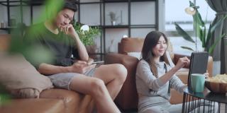 家庭隔离隔离，亚洲夫妇坐在放松使用笔记本电脑和平板电脑社交媒体或网上购物冲浪在客厅的家庭室内背景