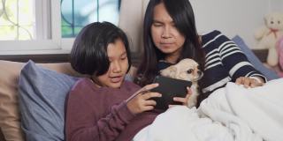 母女二人用平板电脑视频通话，在卧室里和狗狗玩耍。幸福的家庭的概念。