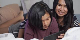 亚洲母亲和孩子一起使用手机。泰国妇女和儿童在家学习在线学习。妈妈和孩子抱着狗玩。新常态生活理念中的幸福家庭。