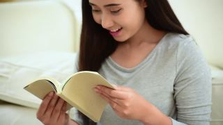 放松的亚洲女人读书坐在客厅的沙发上抱着书读。18、少妇舒心读书，读书开卷休闲心灵。幸福美女人笑脸幸福时光视频素材模板下载
