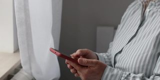 一个女人在客厅的窗户旁用智能手机，手握着键盘在网上交流。
