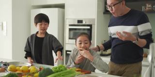 亚洲华人父女在厨房柜台边切橘子边和儿子一起吃饭