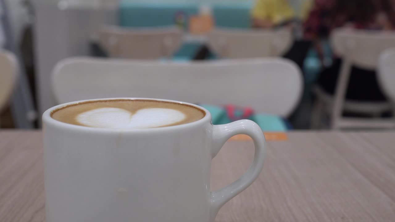 餐馆的木桌上放着一杯咖啡。拉花的形状是心形的。