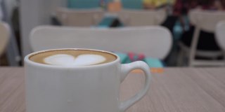 餐馆的木桌上放着一杯咖啡。拉花的形状是心形的。