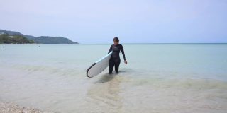 亚洲女人在莽撞的警卫手持冲浪板在海滩上行走