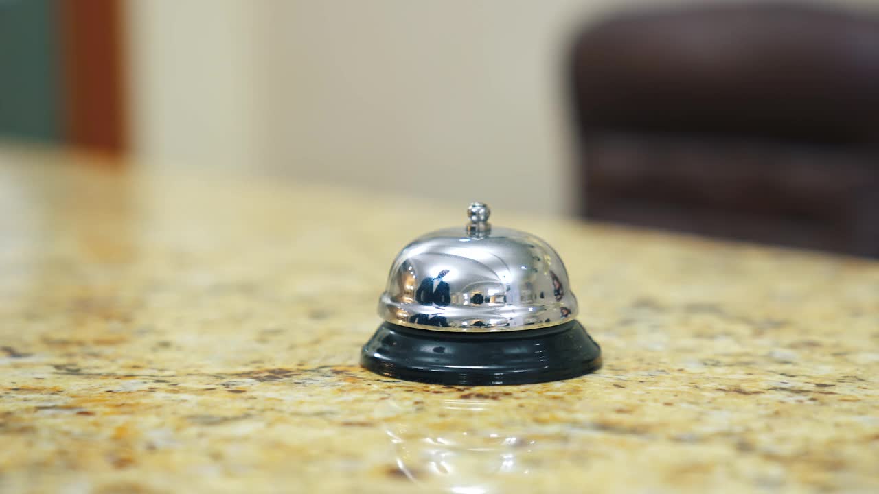 酒店的金属铃按钮。手触碰桌上的电子铃，给旅馆的接待员打电话。特写镜头。