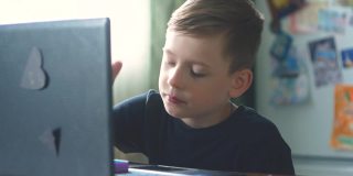 一个白人男孩在课间休息时间坐在家里的笔记本电脑前学习，玩pop it。远程学习学生主题。一个6-8岁的孩子正在用笔记本电脑学习。有选择性的重点