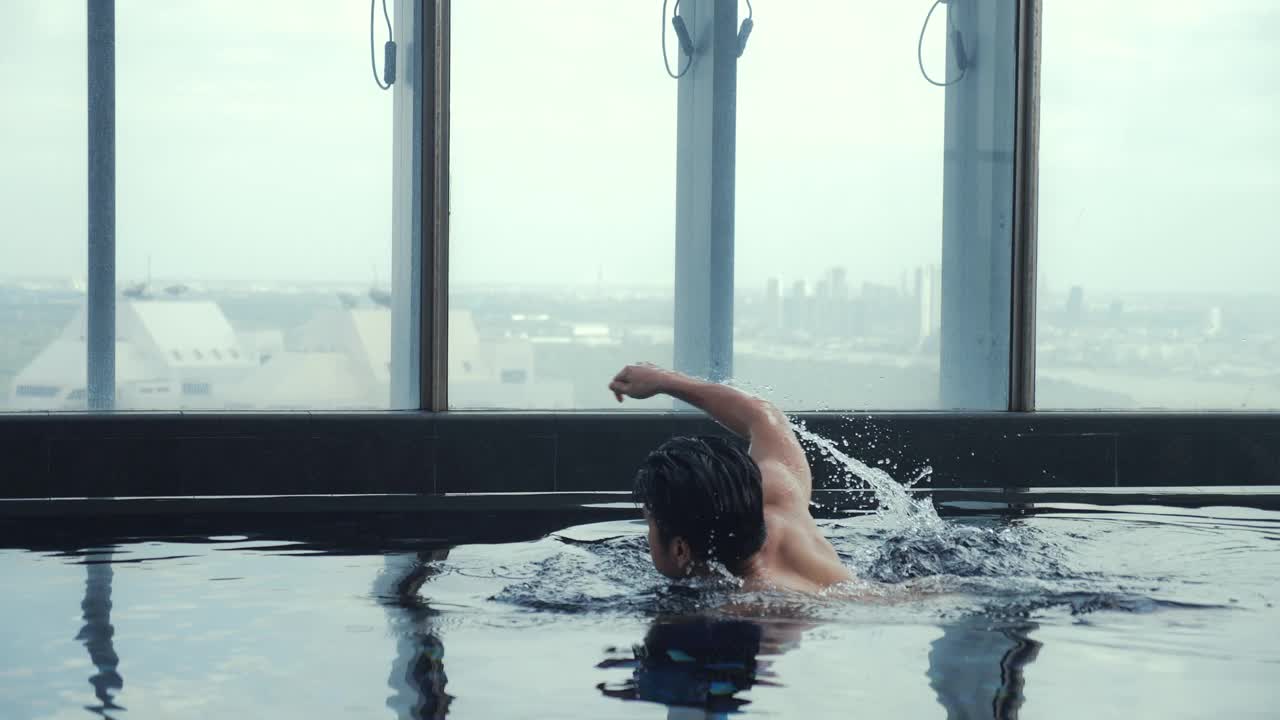 年轻的亚洲人生意游泳前爬行在酒店游泳池与城市景观。慢动作
